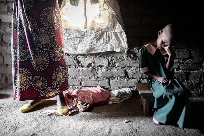 Eleven-year-old Gloria Chipasula sits wearing her school dress as her mother, Teleza James, stands next to her in their home in Nsanje, Malawi. Gloria is both HIV and TB positive.