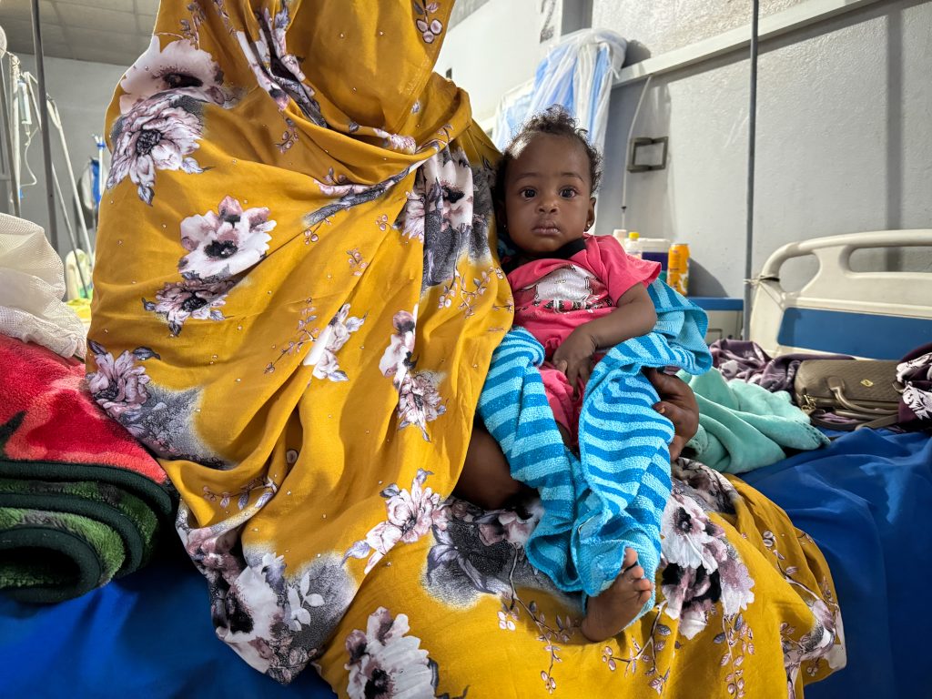 Ferdos holds her 11-month-old baby, Banan, who is infected with measles, in the isolation ward at El Geneina Teaching Hospital, supported by MSF. War forced Ferdos and her family to flee to El Geneina, where they live in overcrowded conditions with other families. Her son contracted measles and infected his 11-month-old daughter.